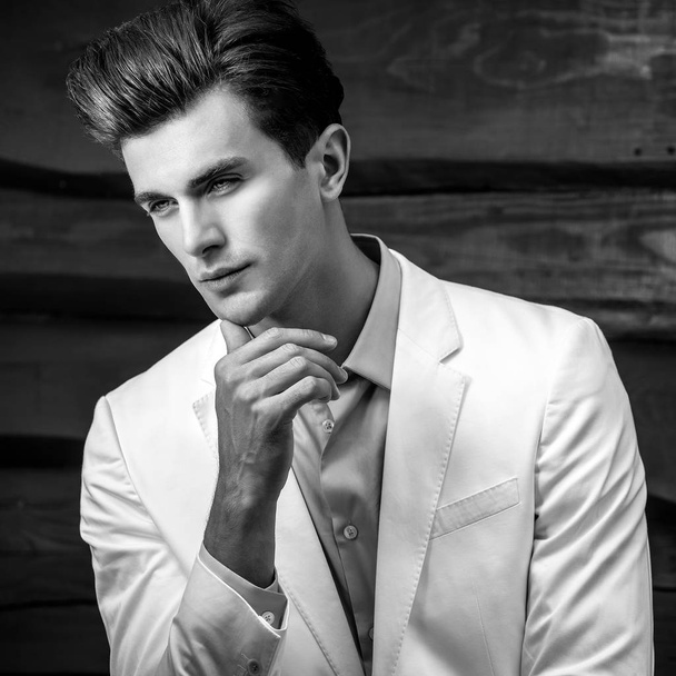 Black-white portrait of young handsome fashionable man in white suit against wooden wall - Фото, зображення