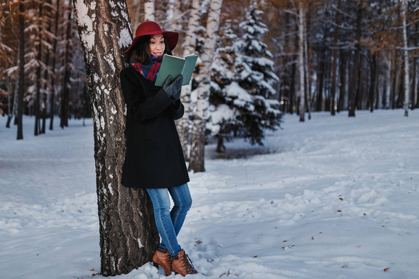 winter street portrait of young beautiful looking woman in classic clothes holding and reading book and smiling. The concept of deep and meaningful soul of a poet - Foto, imagen