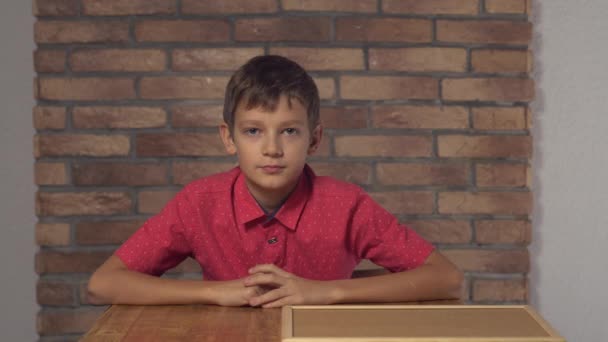 criança sentada na mesa segurando flipchart com letras chefe no fundo parede de tijolo vermelho
. - Filmagem, Vídeo