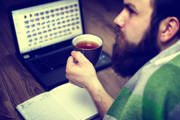 бородатий красивий чоловік лежить на підлозі, загорнутий в плетений, і робочий ноутбук
 - Фото, зображення