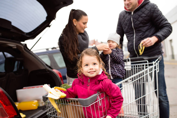 Parents pushing shopping cart with groceries and their daughters - Фото, изображение