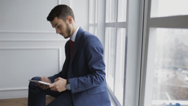 Coworker businessman using digital tablet sitting on windowsill - Felvétel, videó