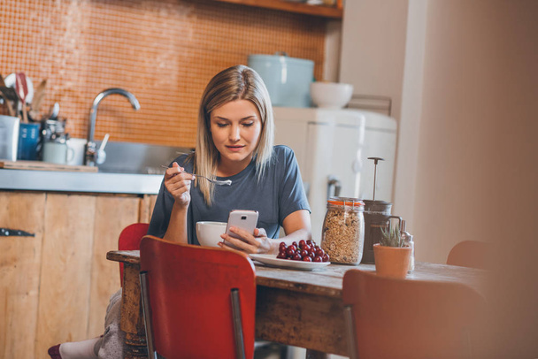 woman sitting at table in kitchen using cellphone - Φωτογραφία, εικόνα