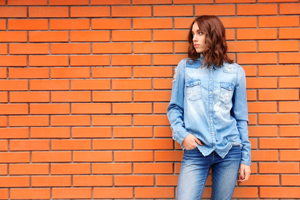 Young woman in casual clothes standing against brick wall - Foto, imagen