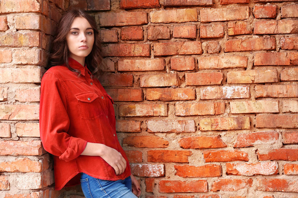 Pretty young woman leaning against brick wall - Foto, imagen