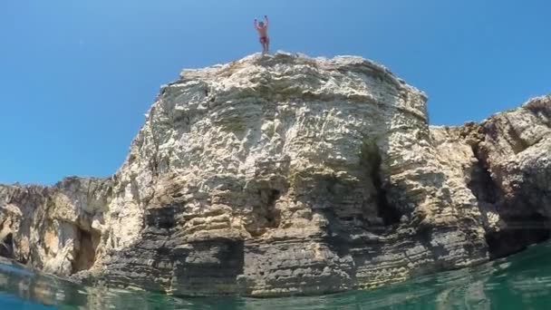 Lassú mozgás közelről alatti: Ember, ki egy nagy tengeri sziklán vízbe ugrás - Felvétel, videó