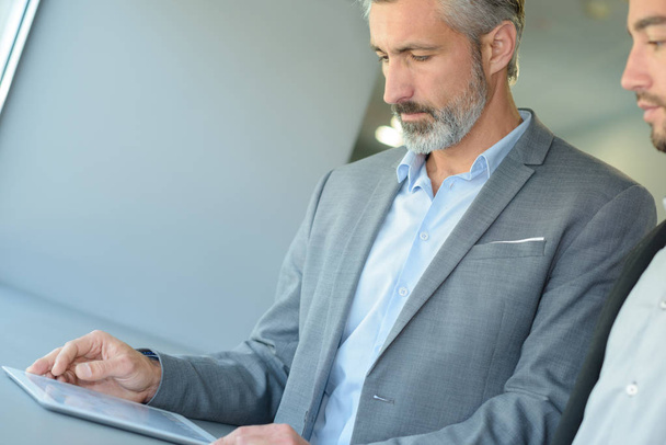 бизнесмен показывает коллеге информацию в планшете
 - Фото, изображение