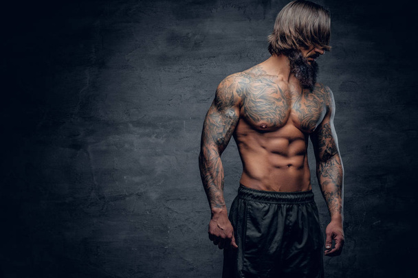 Parrakas mies, jolla on tatuoitu lihaksikas vartalo
 - Valokuva, kuva