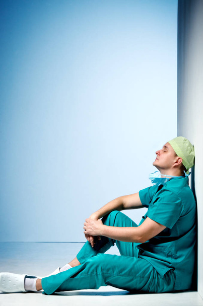 Втомлений лікар сидить на підлозі в коридорі лікарні
. - Фото, зображення