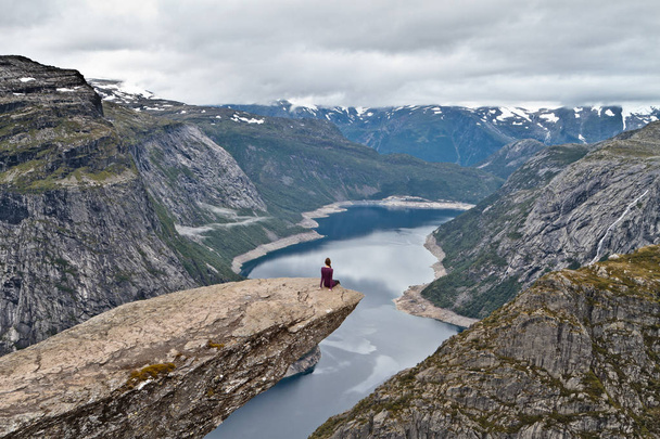 Κορίτσι που κάθεται σε βράχο χώρου (Trolltunga) (Troll του γλώσσα ροκ) και κοιτάζοντας Νορβηγικά ορεινό τοπίο - Φωτογραφία, εικόνα