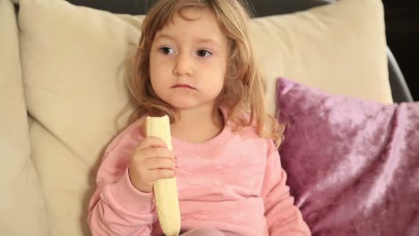 Cute little girl eating  eating a banana - Materiał filmowy, wideo