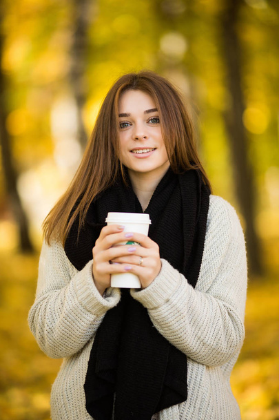 Νεαρό κορίτσι πίνει καφέ στο ηλιόλουστο πάρκο κίτρινο το φθινόπωρο - Φωτογραφία, εικόνα