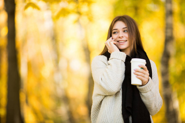 Dziewczyny mówią na telefon z kubkiem kawy w słoneczny żółty park - Zdjęcie, obraz