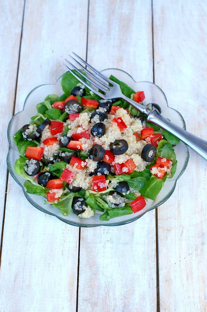 Salada vegan saudável fresca com quinoa, salada de milho, azeitonas pretas, pimenta vermelha e azeite em pano de tigela de vidro em fundo de madeira branca
 - Foto, Imagem