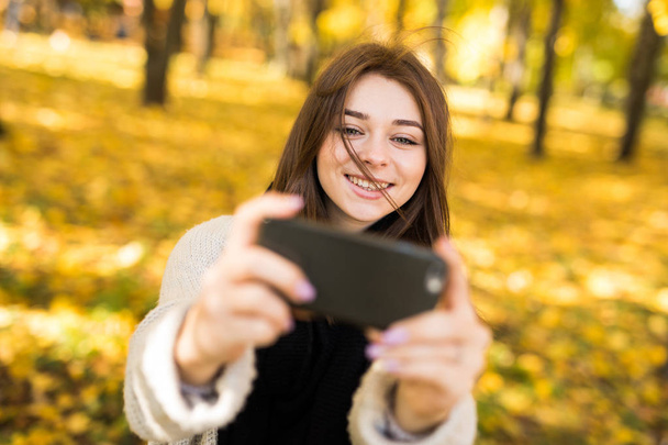 Smile girl taking selfie on mobile phone in sunny autumn park - Foto, afbeelding