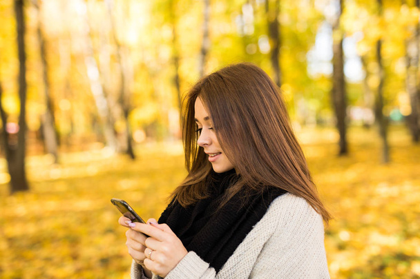 Girl texting on phone in autumn park - Foto, Imagen