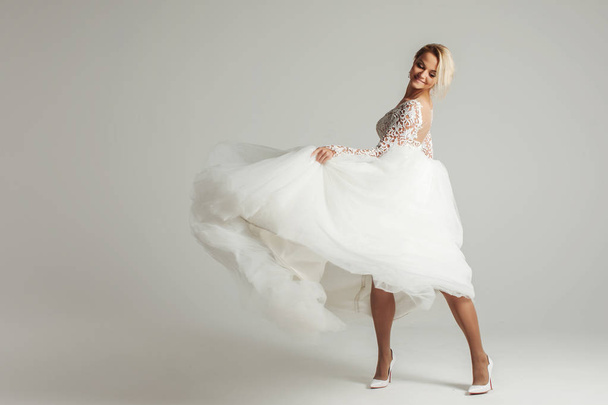 Beautiful attractive bride in wedding dress with long full skirt, white background, dance and smile - Φωτογραφία, εικόνα