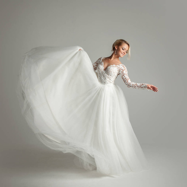 Beautiful attractive bride in wedding dress with long full skirt, white background, dance and smile - Valokuva, kuva