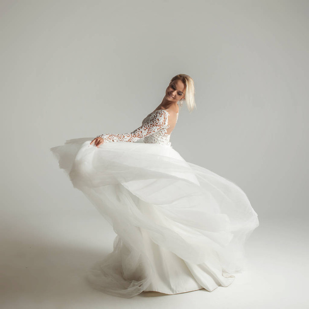 Beautiful attractive bride in wedding dress with long full skirt, white background, dance and smile - Foto, Imagem