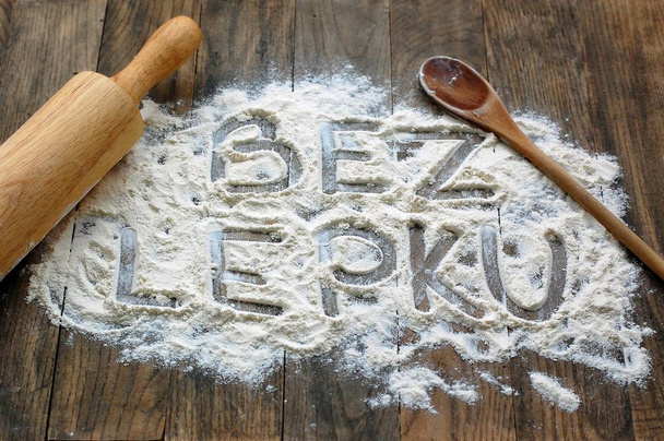Gluten free flour with text gluten free in Czech language with wooden spoon and rolling pin on dark brown wooden background - Photo, Image