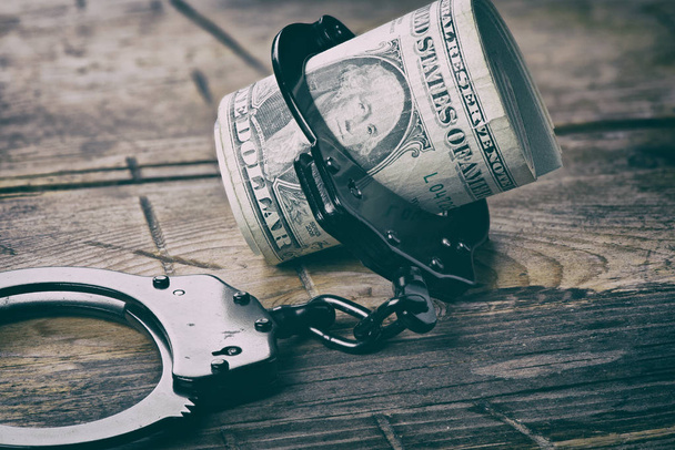 Handcuffs and money on wooden table - Fotoğraf, Görsel