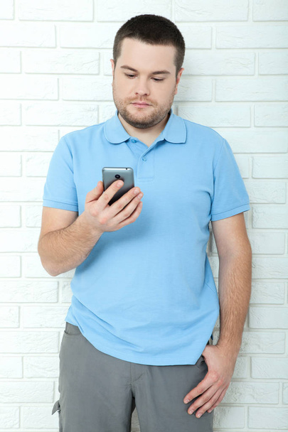 Happy casual man using smartphone standing near brick wall. Young handsome man thought - Foto, immagini