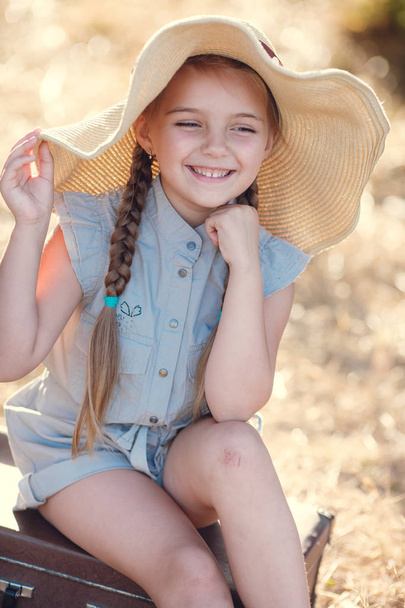 Little girl in a straw hat,resting sitting on a suitcase - Фото, зображення