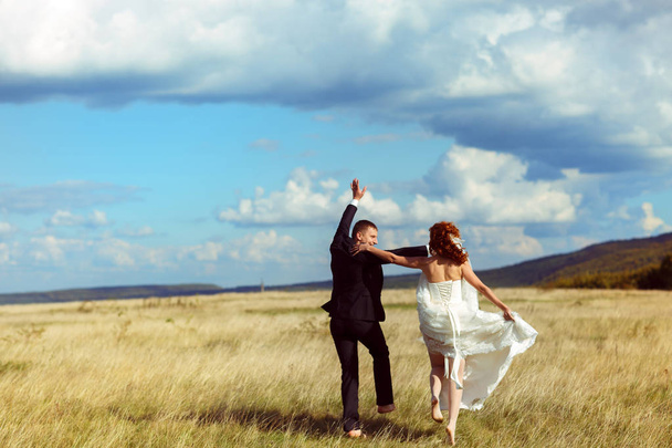 Wedding couple has fun walking along the field in a shiny weathe - Photo, image