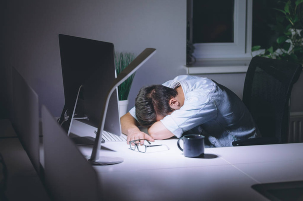 Sleeping young man working on computer at night in dark office - Foto, Bild