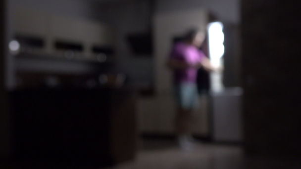 Defocused ember megnyitása hűtőszekrény sötét konyhában. Falánkság és a túlsúly fogalmak. 4k videóinak - Felvétel, videó