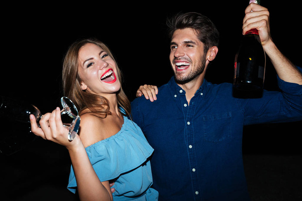 Happy young couple drinking champagne and laughing at night - Photo, Image