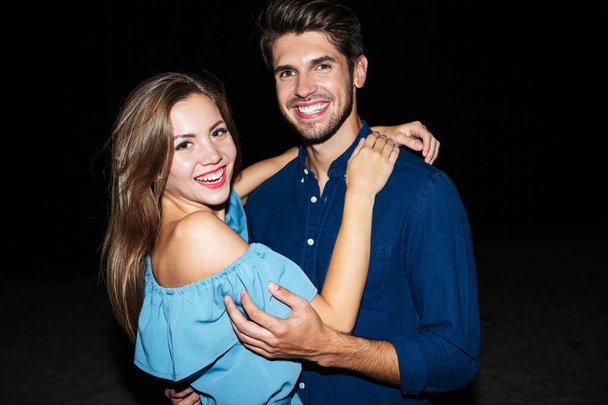 Cheerful beautiful young couple standing on the beach at night - Foto, imagen
