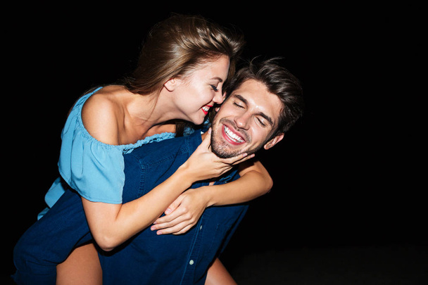 Cheerful young man holding girlfriend on his back at night - Photo, Image