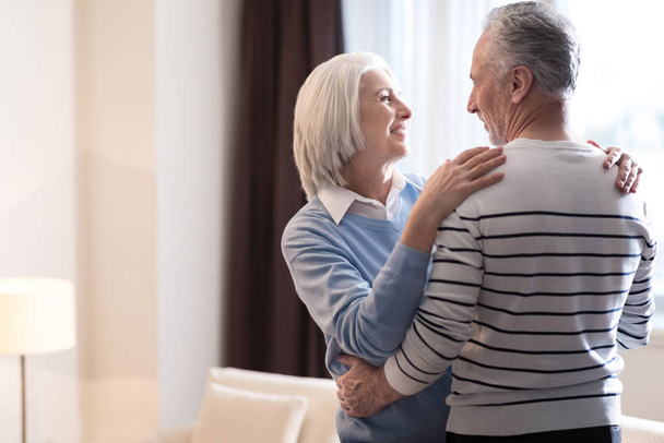Cheerful aged couple hugging each other at home - Фото, изображение