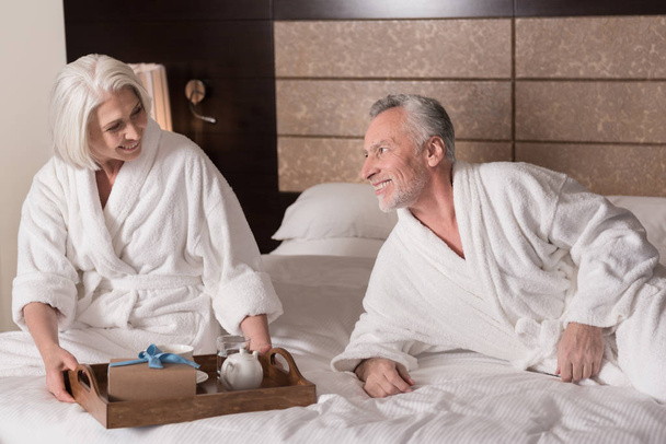 Delighted aged couple having the breakfast on the bed - Foto, afbeelding