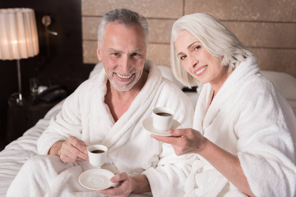 Happy pleasant aged couple drinking coffee on the bed - Фото, зображення