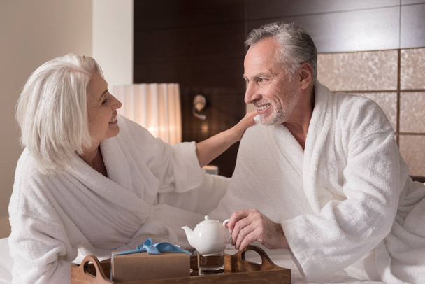 Delighted pleasant couple having drinking tea on the bed - Fotó, kép