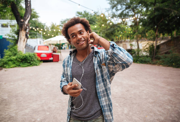 Smiling man in earphones listening to music from cell phone - 写真・画像