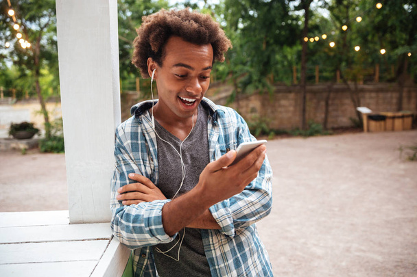 Happy amazed man in earphones using mobile phone outdoors - Foto, imagen