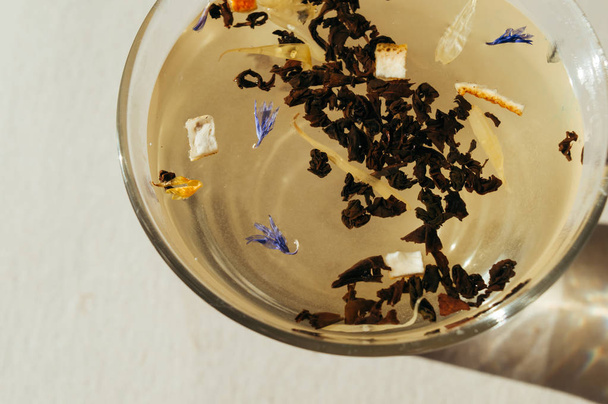 Chá preto com flores azuis, casca de laranja e pétalas em uma transpa
 - Foto, Imagem