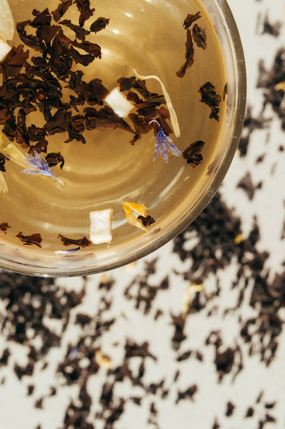 Chá preto com flores azuis, casca de laranja e pétalas em uma transpa
 - Foto, Imagem