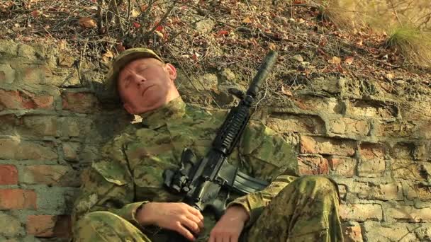  Soldado con rifle automático dormir y despertar cerca de la pared de ladrillo
  - Metraje, vídeo