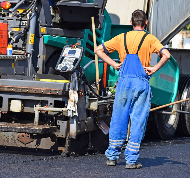 Trabalhador da construção ao lado de um veículo de pavimentação de asfalto
 - Foto, Imagem