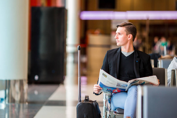 搭乗を待っている間空港で新聞と若い白人男。スーツのジャケットを着てカジュアルな青年実業家. - 写真・画像