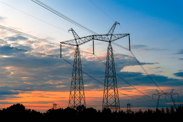 Электрические пилоны на фоне трансформаторной подстанции во время захода солнца. - Фото, изображение