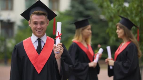 Gelukkig man in academische jurk tonen diploma voor camera en lachen, succes - Video