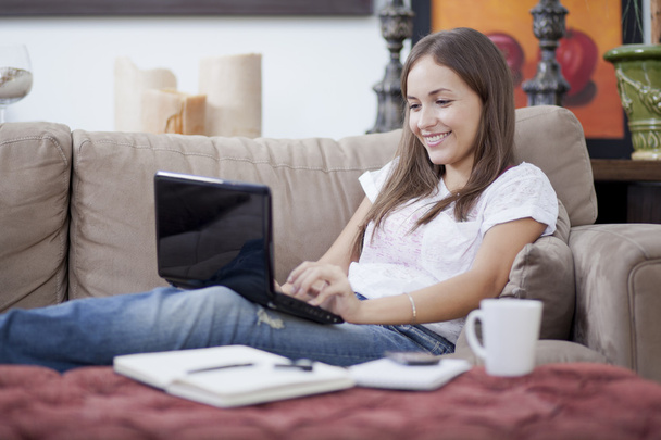 Женщина расслабилась на диване с ноутбуком, кофейной чашкой, ручкой и ноутбуком
 - Фото, изображение