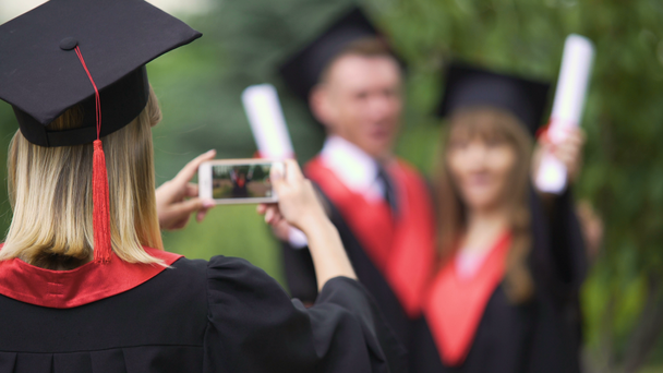 Mujer en vestido académico y sombrero filmando mejores amigos en el teléfono, día de la graduación
 - Imágenes, Vídeo