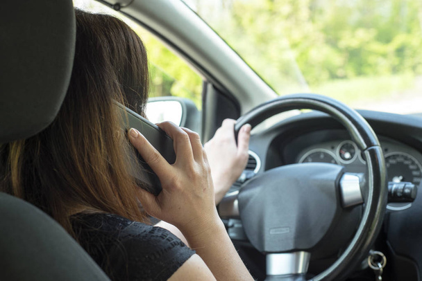 Kobieta kierowca z telefonu komórkowego w dłoni podczas jazdy. - Zdjęcie, obraz