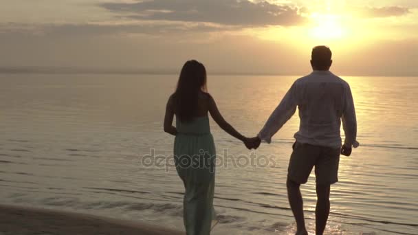 Молода щаслива пара, що гуляє на пляжі на заході сонця. Поняття кохання
. - Кадри, відео